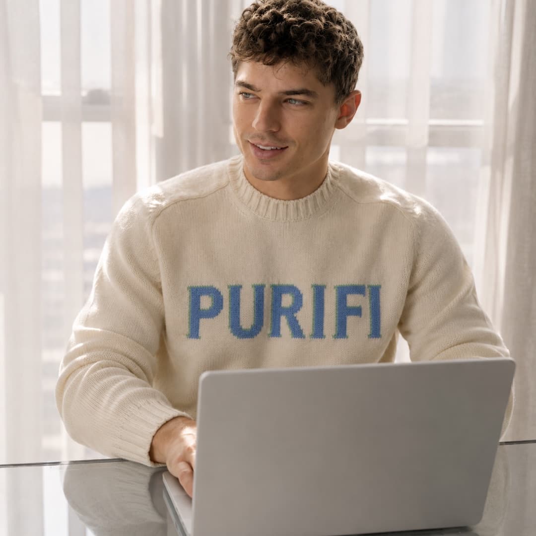 A man working at a laptop by a bright window, looking away from the screen.