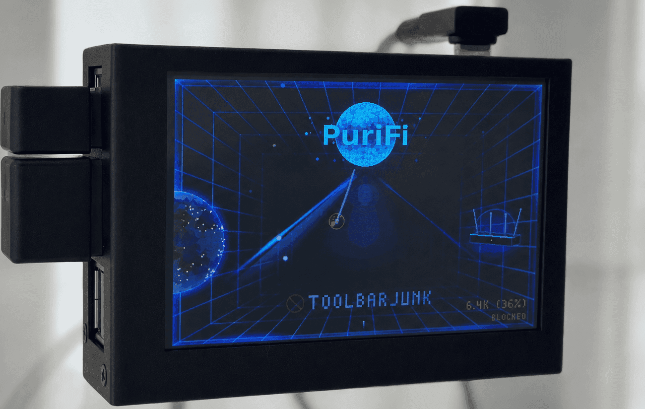 A PuriFi device with its screen lit, showing a blocked company name along the bottom and the day’s blocked count in the corner.