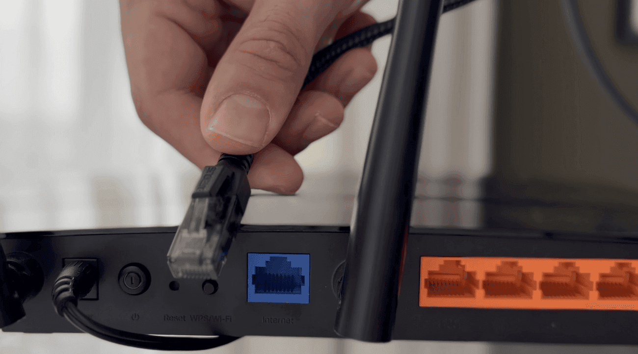 An Ethernet plug going into a router’s odd-coloured Internet port, set apart from the numbered LAN ports beside it.